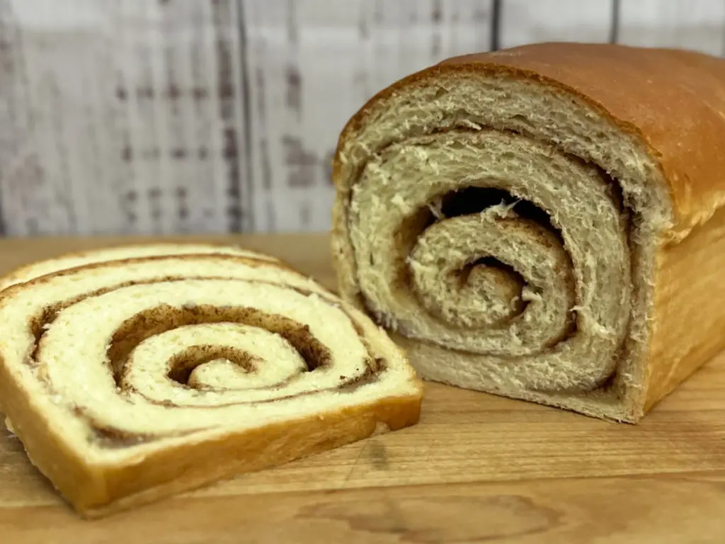 A slice of Cinnamon Swirl Bread alongside a loaf of Cinnamon Swirl Bread.