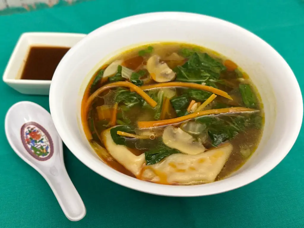 Bowl of Dumpling Soup with spoon and sauce on the side.