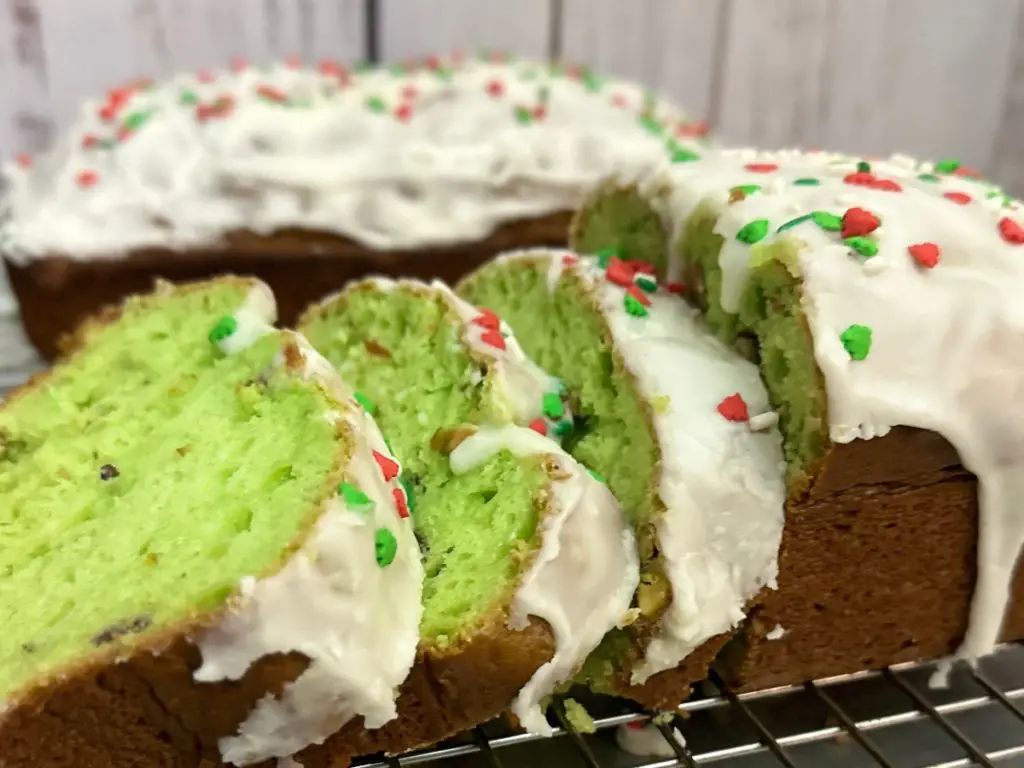 Pistachio Bread slices on a metal cooling rack with a loaf of Pistachio Bread in the background.