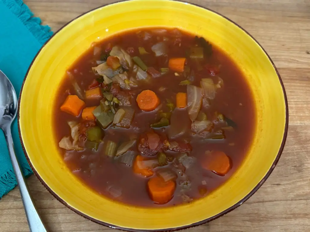 Healthy Diet Cabbage Soup in a yellow ceramic bowl, with a spoon and blue napkin to the side.