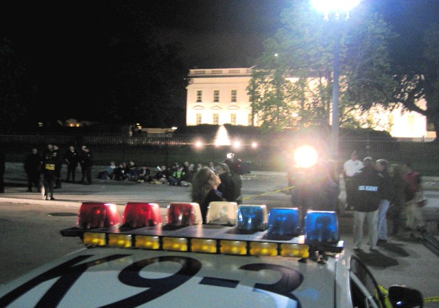 A reporter stands in front of the white house as protesters are arrested in the background on Pennsylvania Ave.