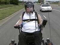 quadriplegic man using vent in his wheelchair and on a trailer behind a motorcycle cruising down an interstate highway