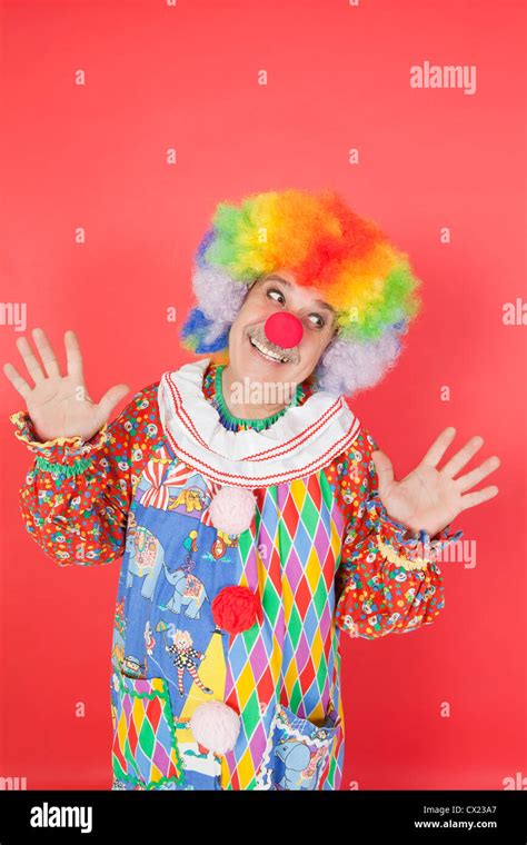 Funny clown with arms raised looking away against colored background ...