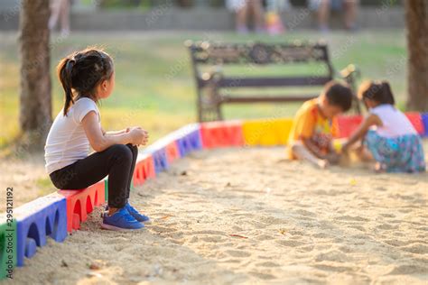 Little girl sitting lonely watching friends play at the playground.The ...