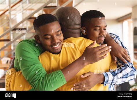 African american senior man and his two sons hugging each other at home ...