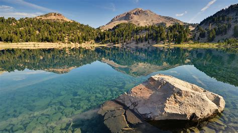 a large rock sitting in the middle of a lake surrounded by trees and ...