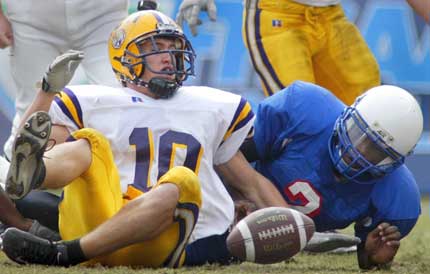 Two opposing football players falling on the grass with a football between them