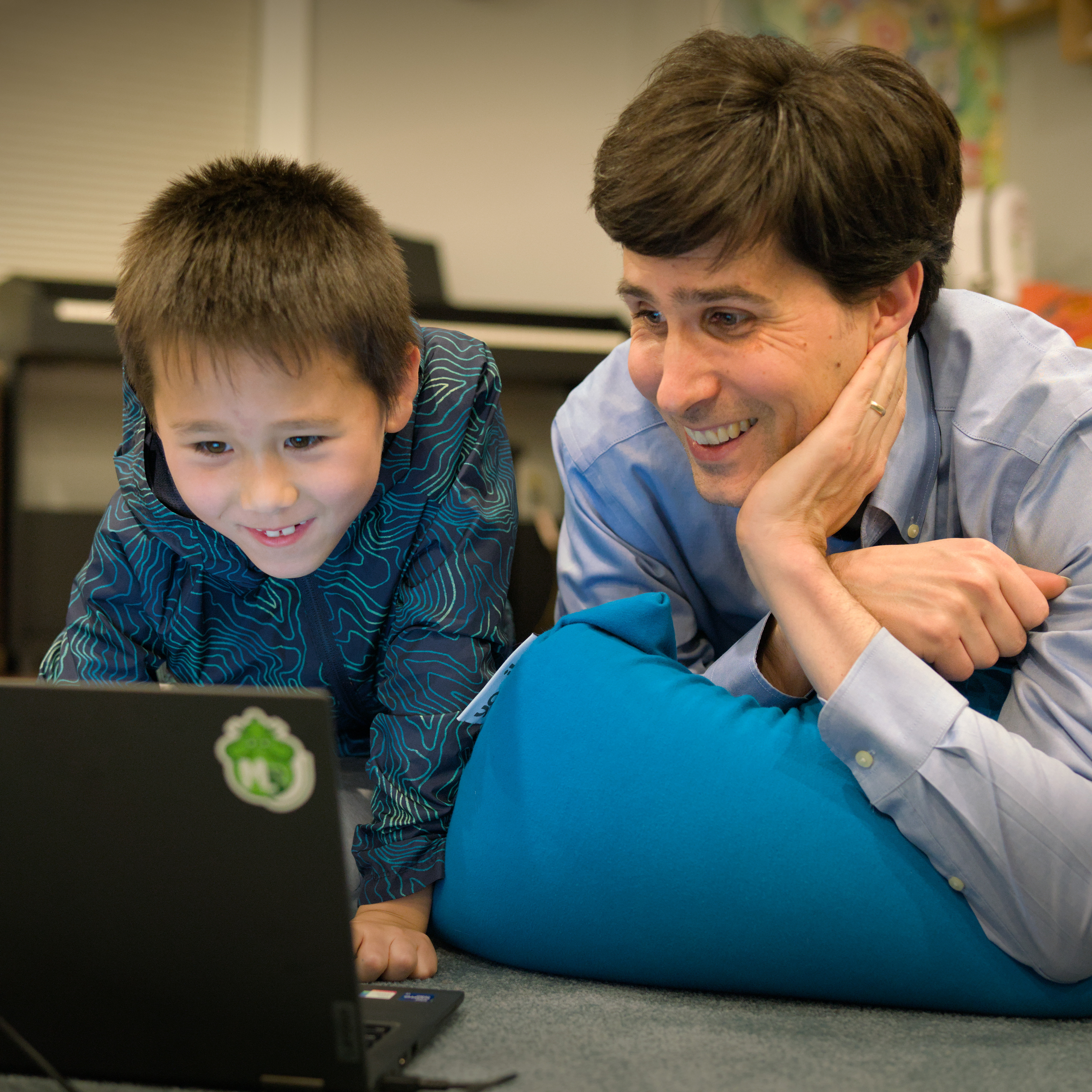 Parent with smiling child, in front of a computer. The Music Blocks logo is visible as a sticker on the computer.